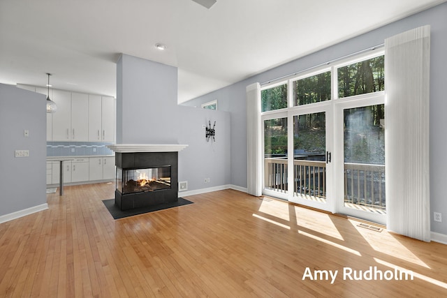 1995 W Glen Ct, Norton Shores, MI 49441 - unfurnished living room with light wood finished floors, a multi sided fireplace, and baseboards