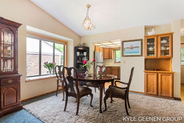 dining area featuring light carpet, lofted ceiling, plenty of natural light, baseboards, and a chandelier