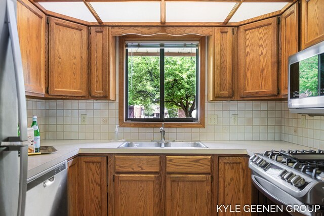 kitchen featuring appliances with stainless steel finishes, a sink, light countertops, brown cabinetry, and tasteful backsplash