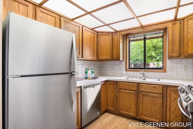 kitchen with appliances with stainless steel finishes, light countertops, a sink, and tasteful backsplash