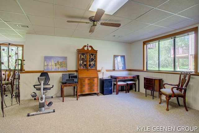 living area featuring carpet flooring, a drop ceiling, ceiling fan, a wainscoted wall, and wooden walls