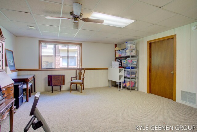 office area featuring carpet floors, a paneled ceiling, a ceiling fan, wooden walls, and a wainscoted wall