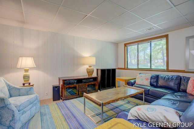 living room with a paneled ceiling, wooden walls, and carpet flooring