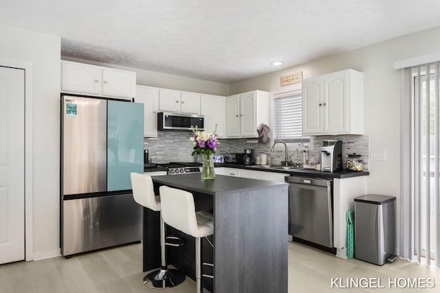 kitchen with stainless steel appliances, dark countertops, light wood finished floors, white cabinetry, and a textured ceiling