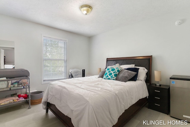 bedroom featuring freestanding refrigerator, a textured ceiling, and wood finished floors