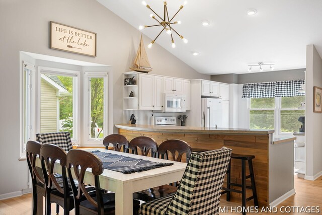 3760 Lakeshore Dr, Holland, MI 49424 - dining space with a chandelier, healthy amount of natural light, light wood-style flooring, lofted ceiling, and baseboards