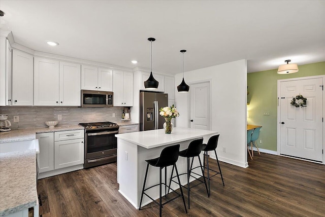 kitchen featuring appliances with stainless steel finishes, dark wood-type flooring, a breakfast bar area, white cabinetry, and recessed lighting