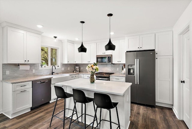kitchen featuring appliances with stainless steel finishes, a sink, dark wood-type flooring, a breakfast bar area, and decorative backsplash