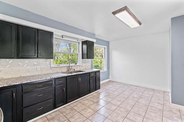kitchen featuring a sink, dark cabinetry, backsplash, light tile patterned flooring, and baseboards
