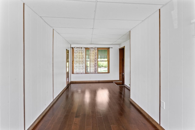 unfurnished room with dark wood-type flooring, a paneled ceiling, and baseboards