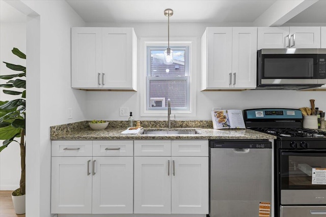 kitchen featuring appliances with stainless steel finishes, a sink, white cabinets, and light stone counters