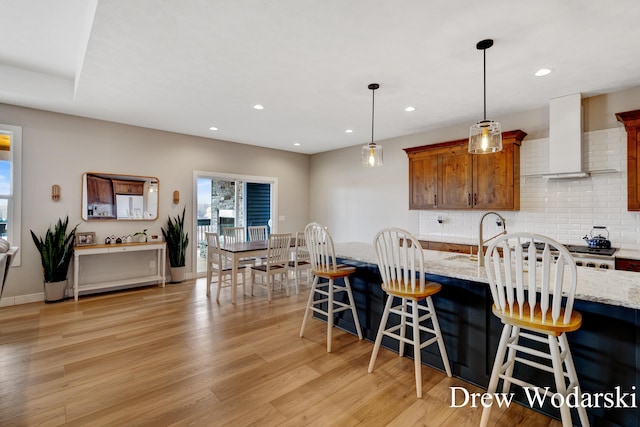 4688 20 Mile Rd, Kent City, MI 49330 - kitchen featuring light wood-type flooring, wall chimney exhaust hood, backsplash, a kitchen bar, and pendant lighting