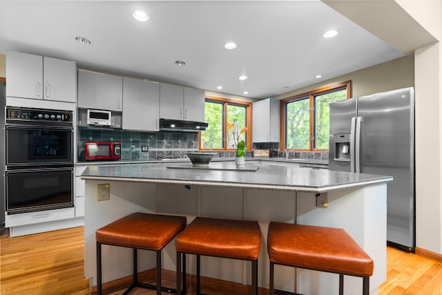 1711 Morton Ave, Ann Arbor, MI 48104 - kitchen with stainless steel fridge with ice dispenser, a kitchen bar, under cabinet range hood, decorative backsplash, and gray cabinetry