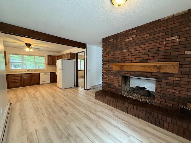 6035 W Trails End Rd, Ludington, MI 49431 - unfurnished living room featuring a baseboard heating unit, a fireplace, a sink, light wood finished floors, and a textured ceiling