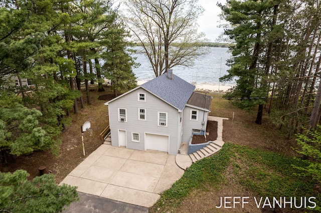 6789 W 76th St, Baldwin, MI 49304 - view of front of property with concrete driveway, an attached garage, a water view, and a shingled roof