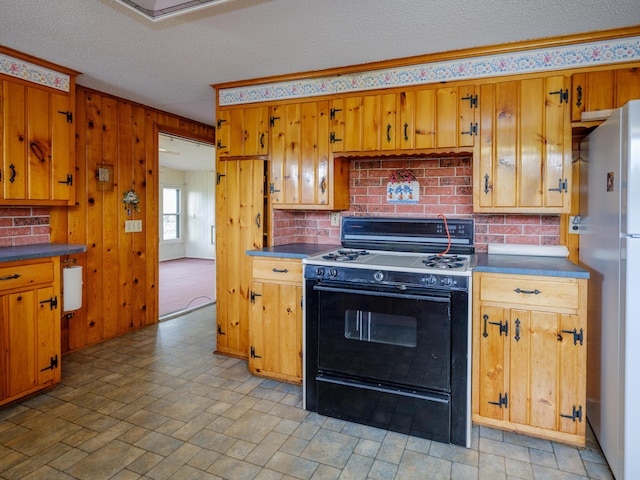 12391 Sunset Dr, Plainwell, MI 49080 - kitchen with black range with gas cooktop, freestanding refrigerator, a textured ceiling, brown cabinetry, and dark countertops
