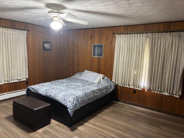 18593 30th Ave, Barryton, MI 49305 - bedroom with a baseboard radiator, wood finished floors, a ceiling fan, and wood walls