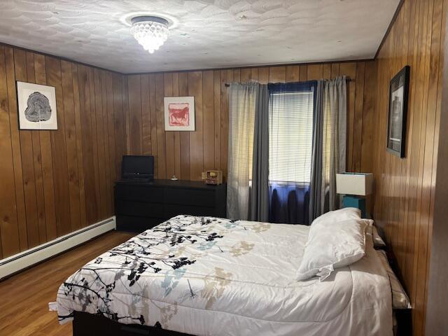 18593 30th Ave, Barryton, MI 49305 - bedroom featuring baseboard heating, wood finished floors, and wooden walls