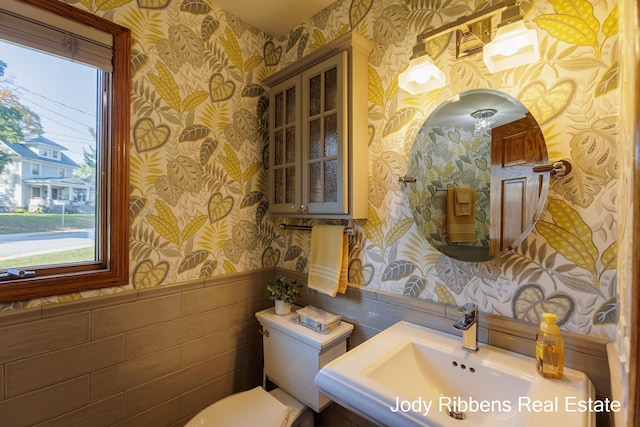 226 Sunset Ave NW, Grand Rapids, MI 49504 - half bathroom featuring wallpapered walls, toilet, plenty of natural light, a wainscoted wall, and tile walls
