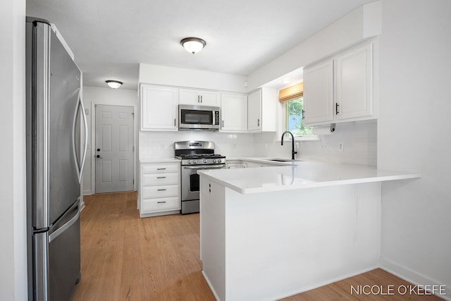 7745 Worthing Ct SW, Byron Center, MI 49315 - kitchen featuring appliances with stainless steel finishes, a peninsula, light wood-style flooring, backsplash, and white cabinetry