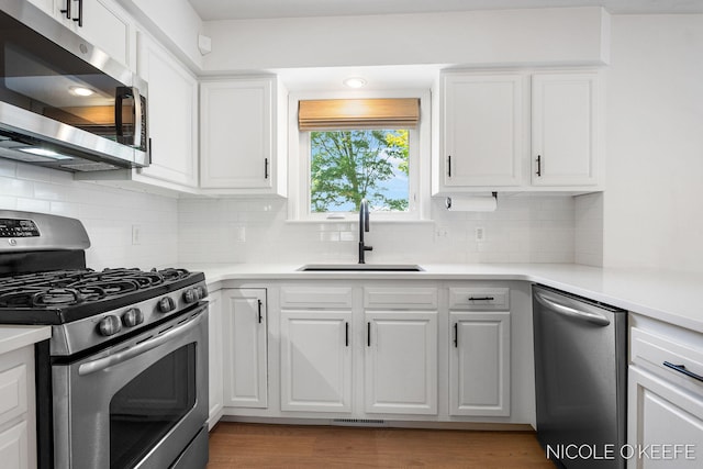 7745 Worthing Ct SW, Byron Center, MI 49315 - kitchen with stainless steel appliances, white cabinetry, light wood-type flooring, and tasteful backsplash