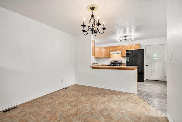 70025 Union Rd, Union, MI 49130 - kitchen featuring a chandelier, freestanding refrigerator, stainless steel gas stove, under cabinet range hood, and light stone finish flooring