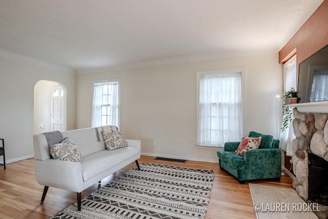 839 Joslin St SE, Grand Rapids, MI 49507 - living area featuring light wood-style floors, arched walkways, a stone fireplace, a textured ceiling, and baseboards