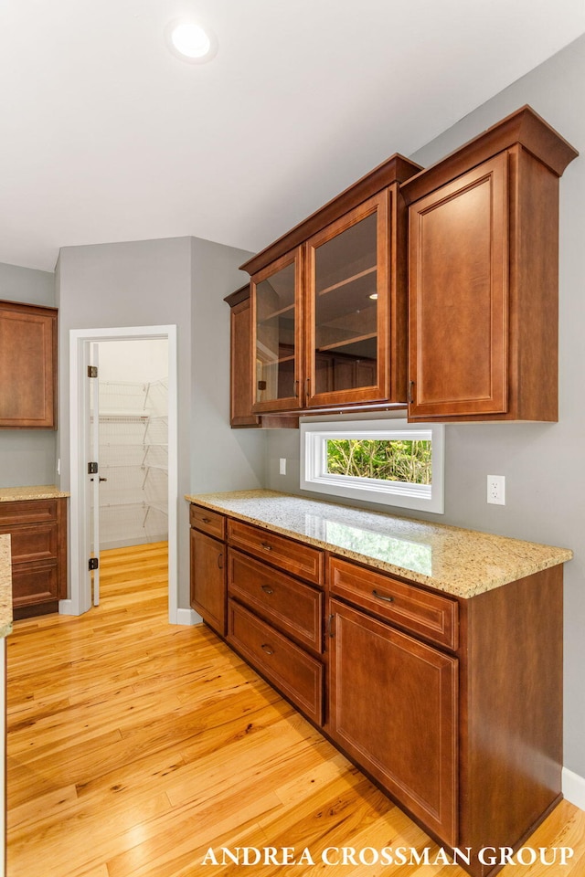 17946 Robbins Rd, Grand Haven, MI 49417 - kitchen featuring light wood-style flooring, light stone countertops, glass insert cabinets, brown cabinets, and recessed lighting