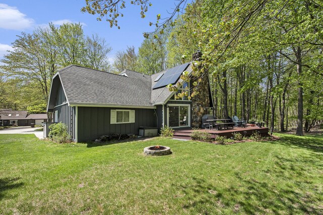 9787 Center Ln, Canadian Lakes, MI 49346 - back of property with a fire pit, board and batten siding, a chimney, solar panels, and a lawn
