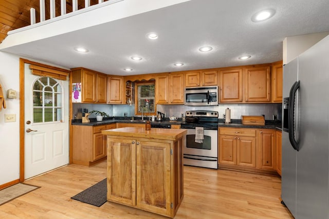13341 Clausen Rd, Trufant, MI 49347 - kitchen featuring appliances with stainless steel finishes, light wood-style floors, a kitchen island, tasteful backsplash, and brown cabinets