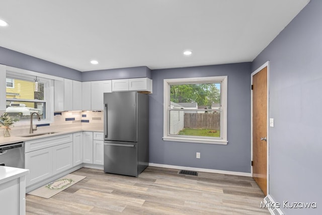 945 NW Dorothy St NW, Grand Rapids, MI 49504 - kitchen featuring stainless steel appliances, a sink, white cabinets, light countertops, and backsplash
