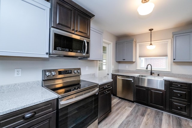481 Gilson St, Coloma, MI 49038 - kitchen featuring appliances with stainless steel finishes, a sink, light wood-style flooring, decorative light fixtures, and light stone counters