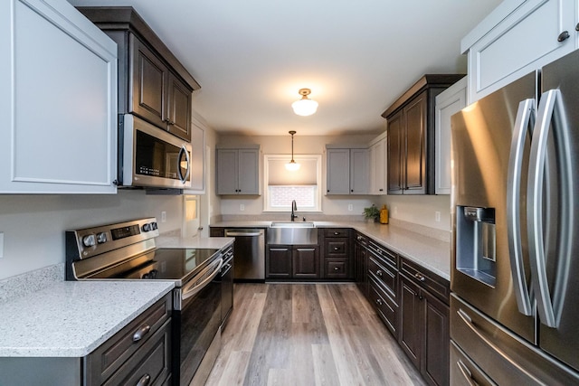 481 Gilson St, Coloma, MI 49038 - kitchen featuring appliances with stainless steel finishes, a sink, light wood finished floors, dark brown cabinetry, and pendant lighting