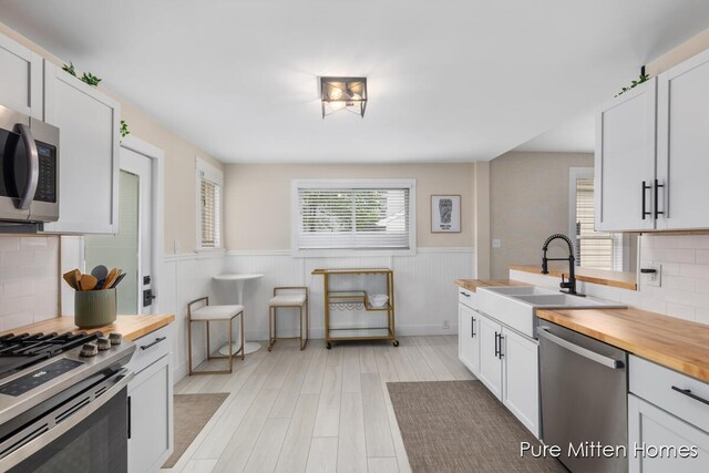 912 Arianna St NW, Grand Rapids, MI 49504 - kitchen with appliances with stainless steel finishes, butcher block counters, a sink, wainscoting, and light wood-type flooring