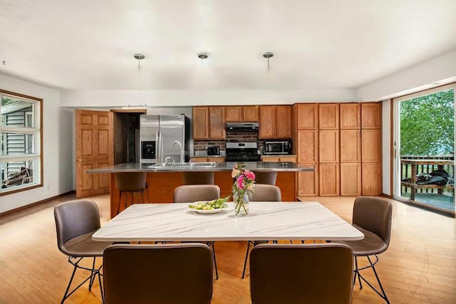 4771 S Lakeshore Dr, Ludington, MI 49431 - kitchen featuring appliances with stainless steel finishes, under cabinet range hood, brown cabinets, an island with sink, and decorative backsplash