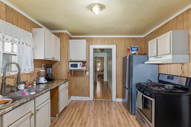 2113 Palace Ave SW, Grand Rapids, MI 49507 - kitchen with stainless steel gas range oven, under cabinet range hood, a sink, light wood-style floors, and wooden walls