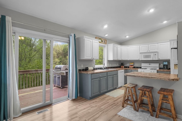 121 W Calgary Dr, Hastings, MI 49058 - kitchen featuring white appliances, white cabinetry, light wood-style flooring, a kitchen bar, and lofted ceiling