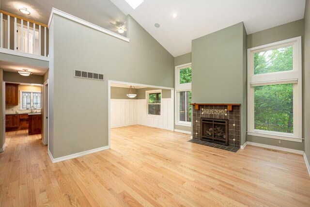4936 Ravine Ct, Ann Arbor, MI 48105 - unfurnished living room featuring high vaulted ceiling, light wood-type flooring, plenty of natural light, a tile fireplace, and a skylight