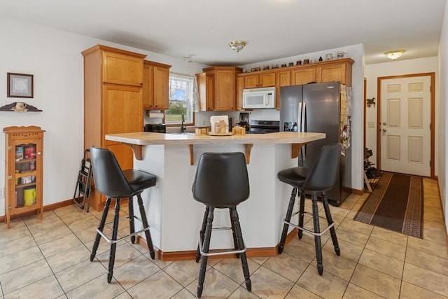 3025 Shawnee Rd, Bridgman, MI 49106 - kitchen featuring appliances with stainless steel finishes, a sink, light countertops, light tile patterned floors, and a breakfast bar area