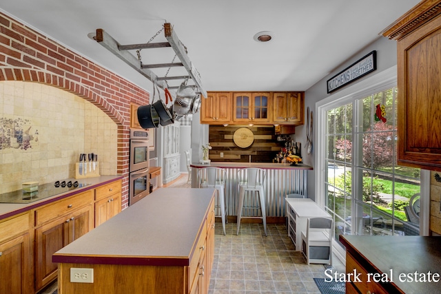300 N 2nd Ave, Fruitport, MI 49415 - kitchen featuring black electric stovetop, decorative backsplash, stainless steel double oven, brown cabinets, and glass insert cabinets