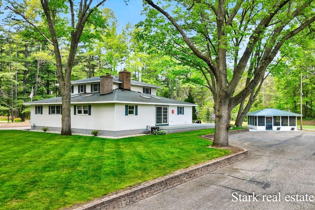300 N 2nd Ave, Fruitport, MI 49415 - view of front facade with a sunroom, a chimney, a shingled roof, a front yard, and driveway