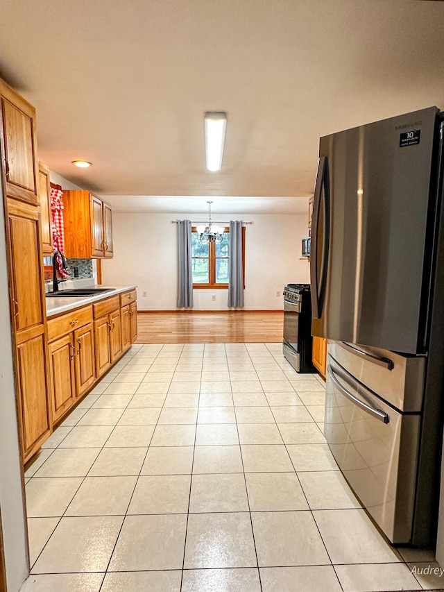 4307 N Mac Rd, Irons, MI 49644 - kitchen with freestanding refrigerator, black range with gas stovetop, a sink, light tile patterned floors, and a chandelier