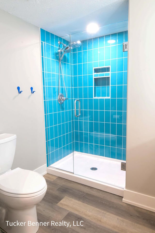 239 Monroe Ave, Muskegon, MI 49441 - bathroom featuring toilet, a stall shower, baseboards, wood finished floors, and a textured ceiling