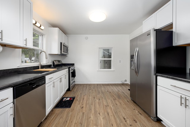 115 Mckinley St, Chelsea, MI 48118 - kitchen with stainless steel appliances, dark countertops, white cabinets, a sink, and light wood-style flooring