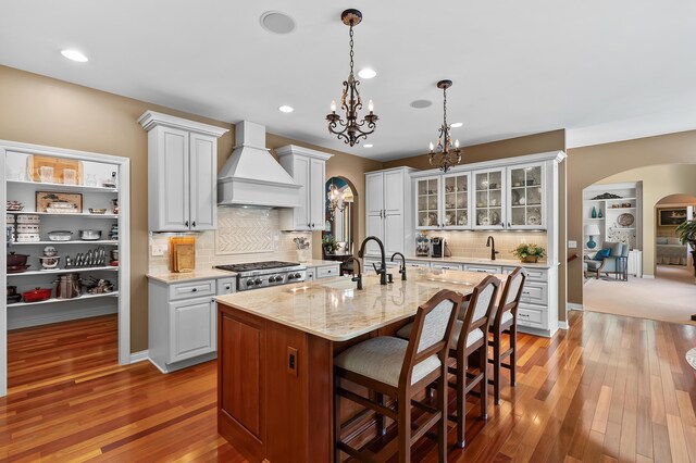 6461 E Bay Ln, Richland, MI 49083 - kitchen featuring custom exhaust hood, arched walkways, a chandelier, a breakfast bar area, and backsplash