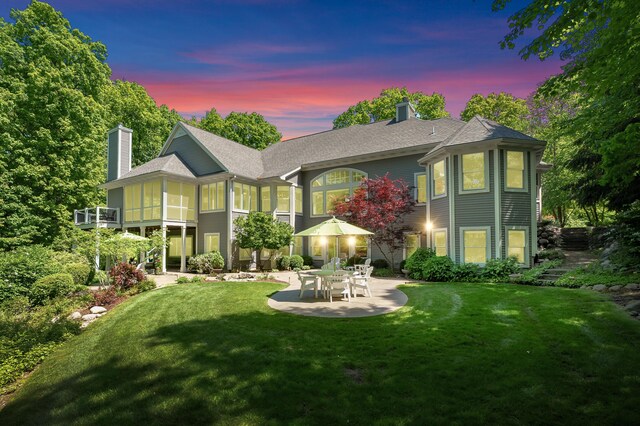 6461 E Bay Ln, Richland, MI 49083 - back of house at dusk with a chimney, a patio, a lawn, and roof with shingles