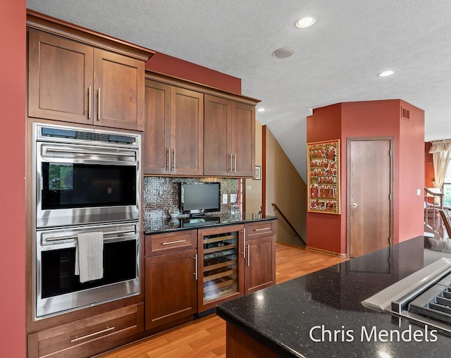 150 Bay Circle Dr, Holland, MI 49424 - kitchen with beverage cooler, double oven, a textured ceiling, light wood-style flooring, and dark stone countertops