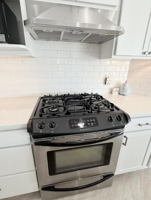 3633 Marina View Pt, Muskegon, MI 49441 - kitchen featuring stainless steel range with gas cooktop, exhaust hood, white cabinets, decorative backsplash, and light wood finished floors