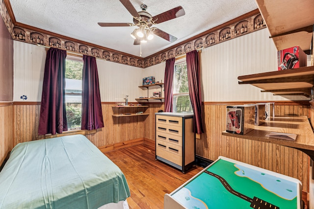 8661 Elm Valley Rd, Union Pier, MI 49129 - bedroom featuring hardwood / wood-style floors, a textured ceiling, baseboards, wood walls, and a ceiling fan
