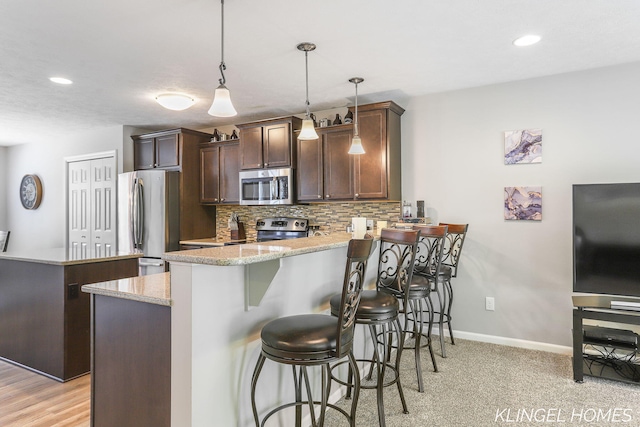926 N Sandalwood Cir, Muskegon, MI 49441 - kitchen with appliances with stainless steel finishes, a peninsula, decorative backsplash, a breakfast bar, and light stone countertops